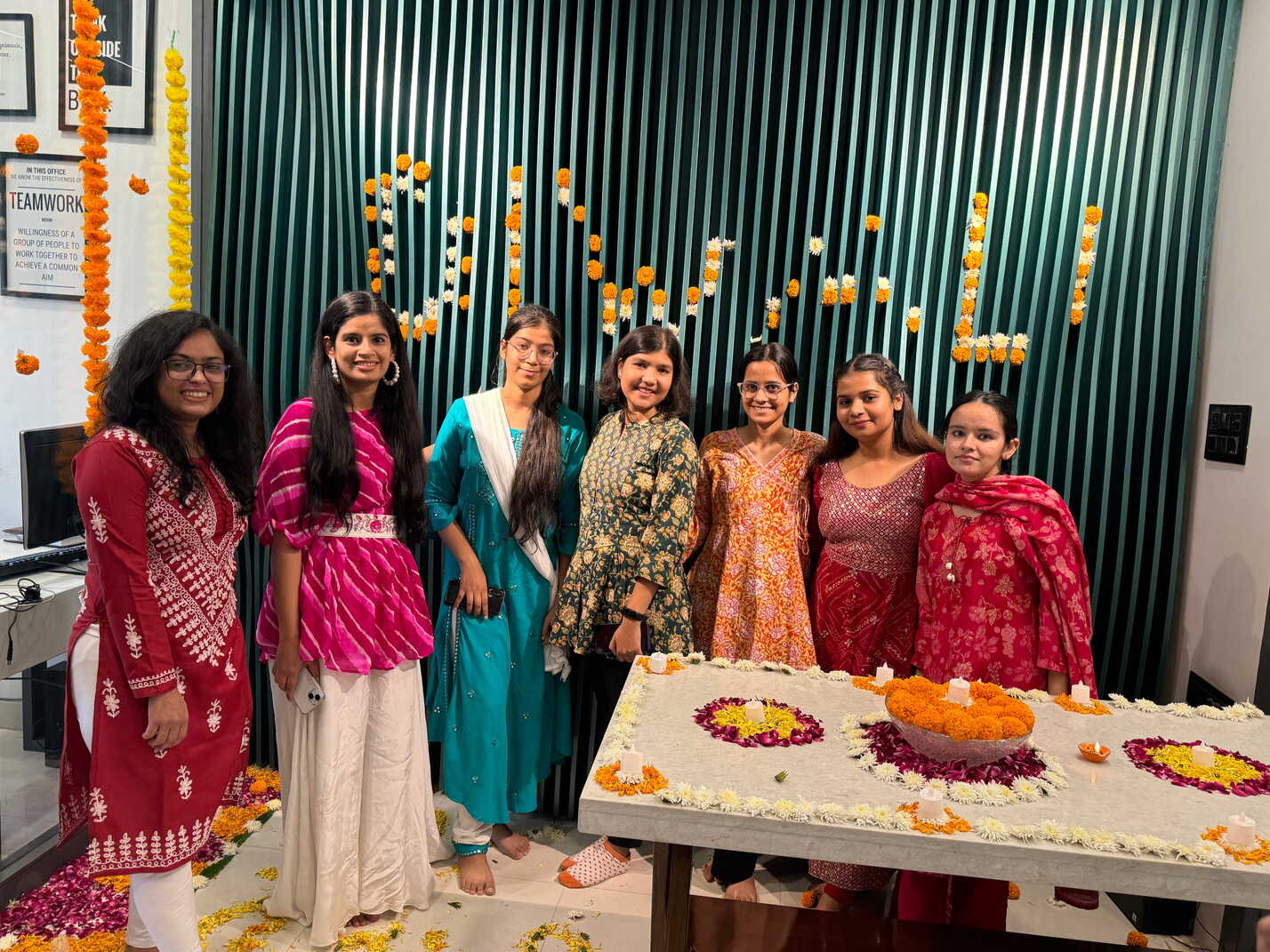 The team celebrating a festival in the office beside a floral rangoli