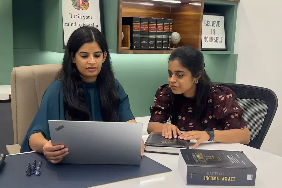 Two colleagues at a laptop with a copy of the Income Tax Act on the desk